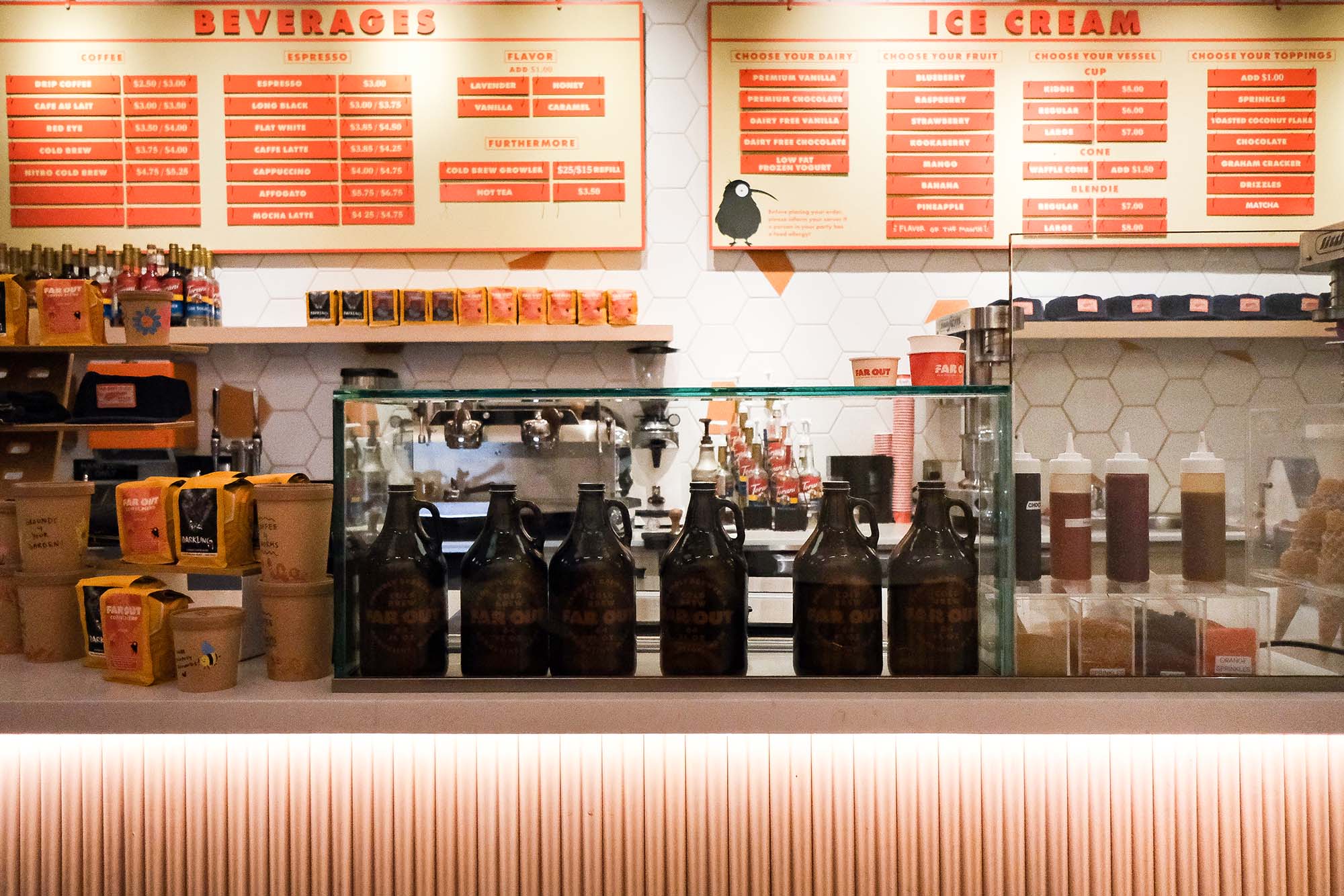 Photo: the interior of Far Out Ice Cream. A burnt orange-themed ice cream and coffee service. Orange menus give choices for coffee and ice cream. Ice cream choices and espresso machine are seen on the counter.