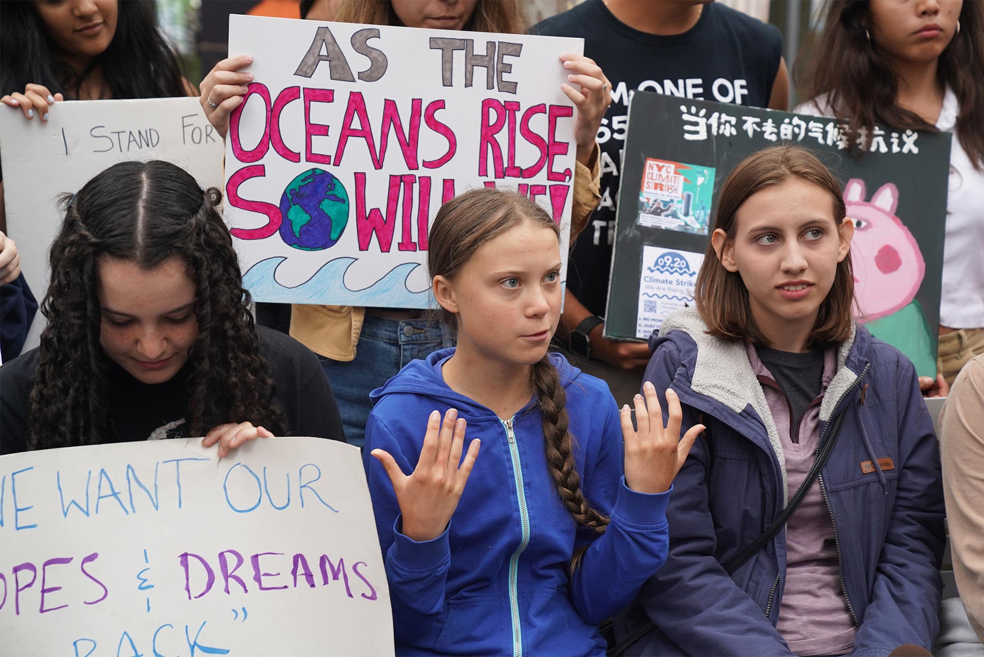 Greta Thunberg talks at protest outside the United Nations surrounded by other climate change protesters holding signs.