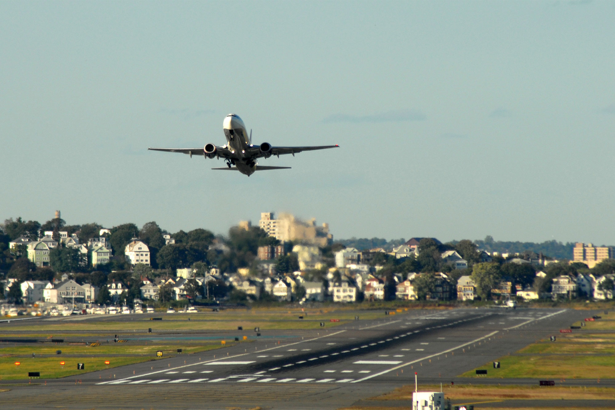 An airplane takes off from Logan International Airport in Boston with a local community visible in the background.