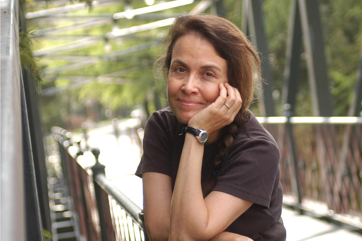 Poet Naomi Shihab Nye smiles for a photo while standing on a bridge