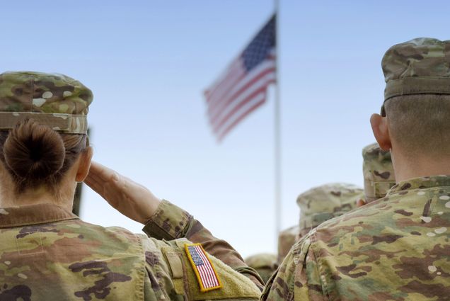 A woman and a man in army uniforms salute the American flag