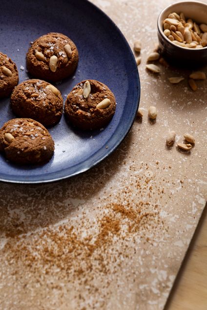 A pate of peanut butter cookies topped with roasted peanuts