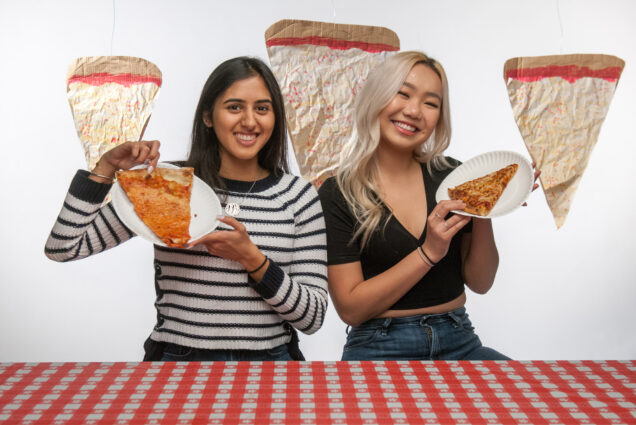 Divya Advani (CGS’18, COM’20) and Jiayi Ma (CFA’20) hold up slices of pizza for a pizza taste test