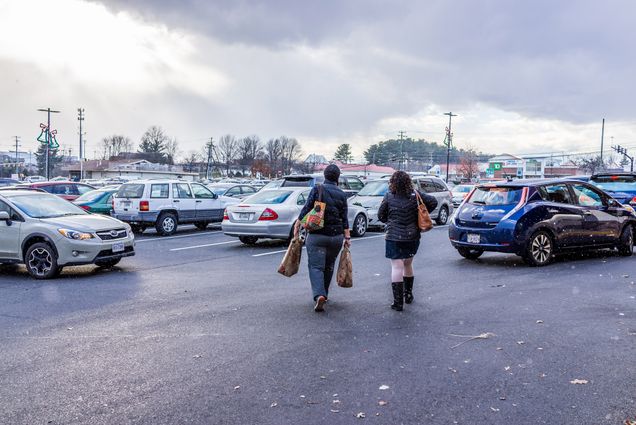 Two women walk through a crowded parking lot while it is snowing