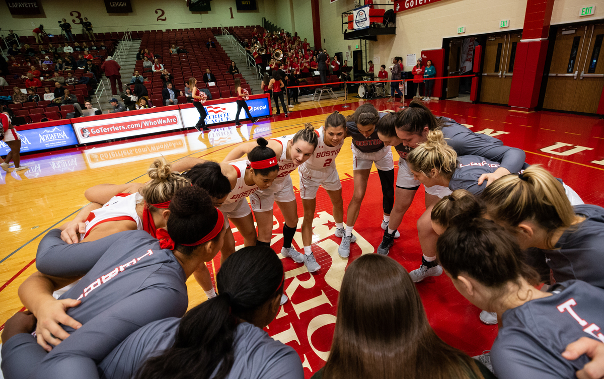 The women's basketball team gathers on the basketball court in a huddle