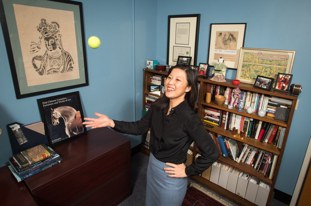 A photo of Alice Tseng standing in her office throwing a tennis ball up in the air