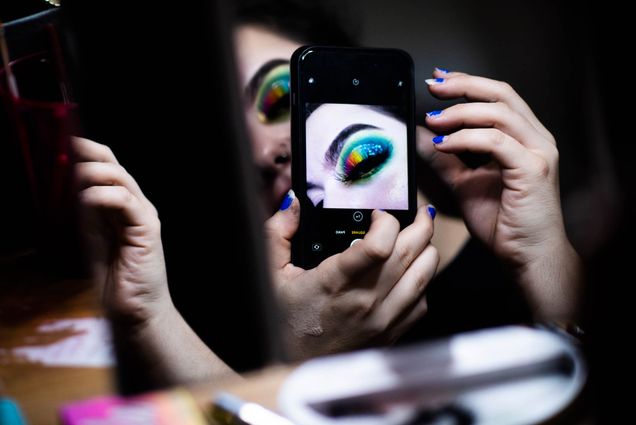 A woman wearing make up takes a photo of her eye with an iPhone.