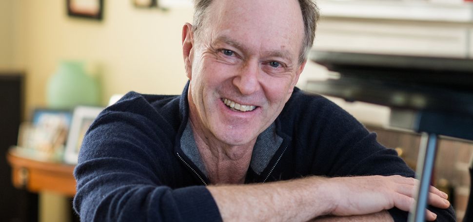 A portrait photo of John Finbury (CAS’77) sitting at his piano.