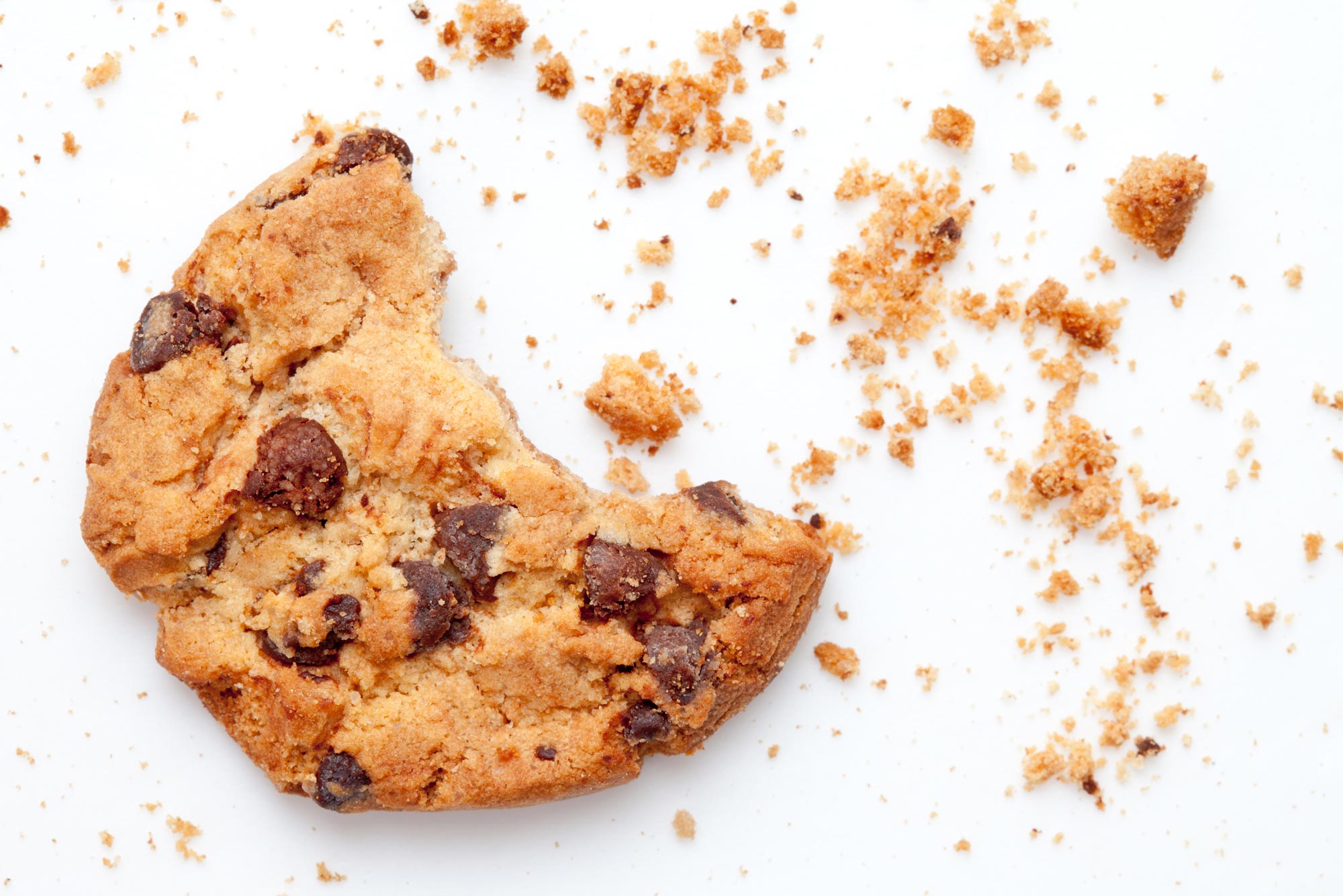 A photo of a cookie with a bite taken out of it and crumbs around it.
