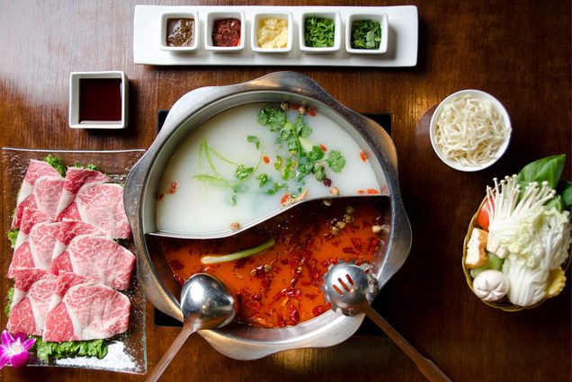 Overhead photo of hot pot with dishes of vegetables, meat slices, and toppings around the central pot.