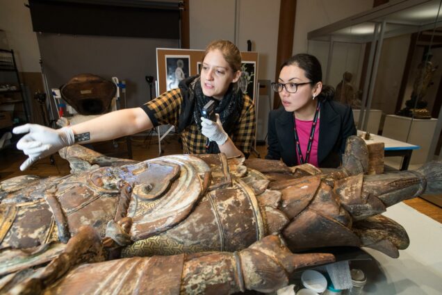 Photo of Christina Yu Yu (GRS'04), the Matsutaro Shoriki Chair of Asian Art (right) examining the sculpture Bishamoten, the Guardian of the North, with MFA associate conservator Linsly Boyer (left) in a conservation lab.