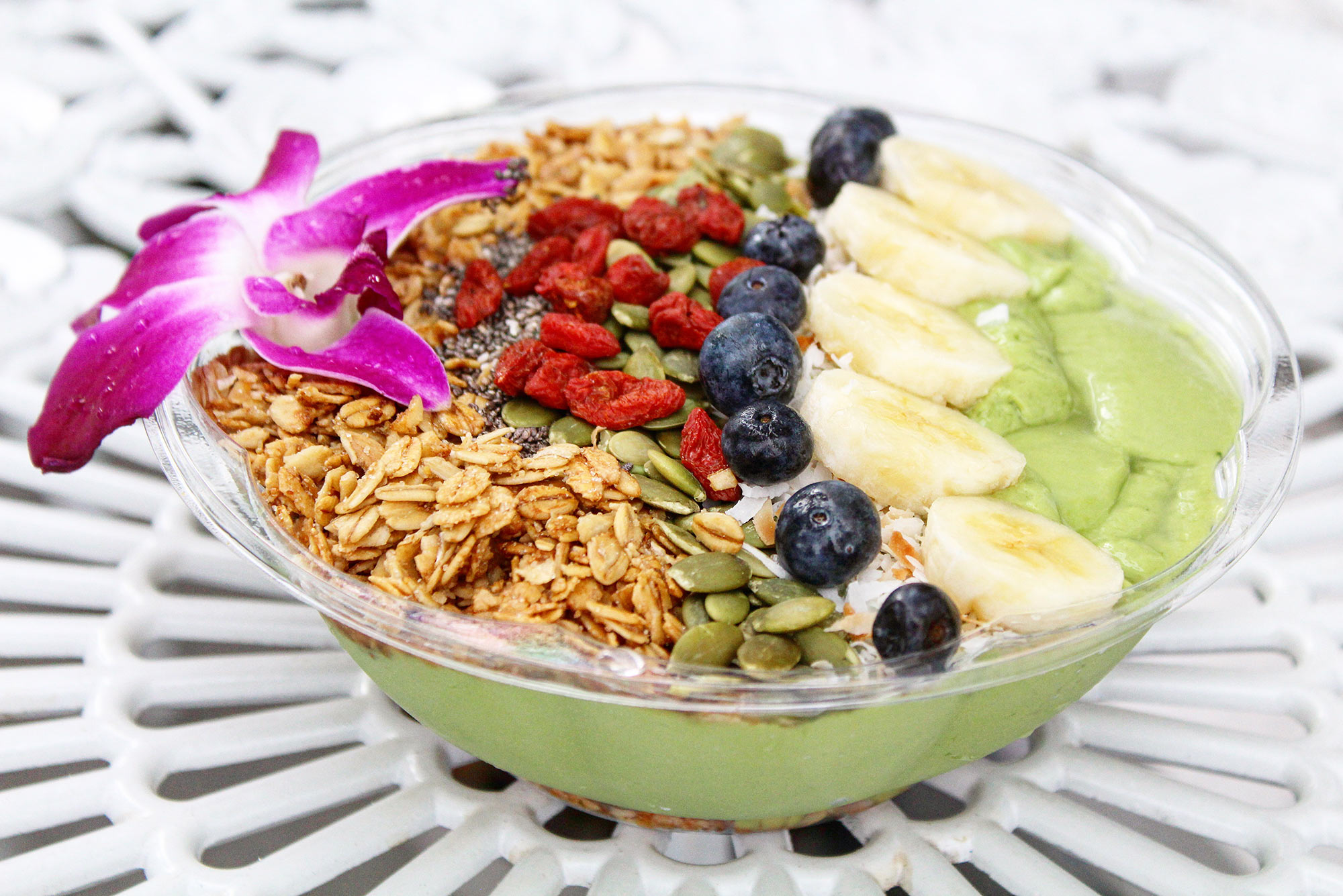 Acai bowl with granola, seeds, and fruit; garnished with a flower.