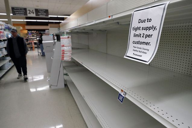 A passerby walks down an aisle with empty shelves where paper towels are normally on display at a grocery store, Thursday, March 26, 2020, in Quincy, Mass. A sign on the shelf says "due to tight supply, limit 2 per customer."