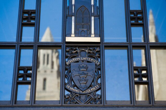 Photo of the entrance to STH with the BU Logo ("Boston University, Learning, Virtue, Piety") with the CAS tower reflected on the left and right.