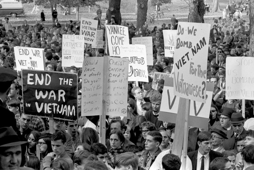 Black and white image taken of BU students and others rally against the Vietnam War in 1970.  Many handwritten signs are seen, including "Do we bomb Vietnam for the Vietnamese?" and "End the war in Vietnam."