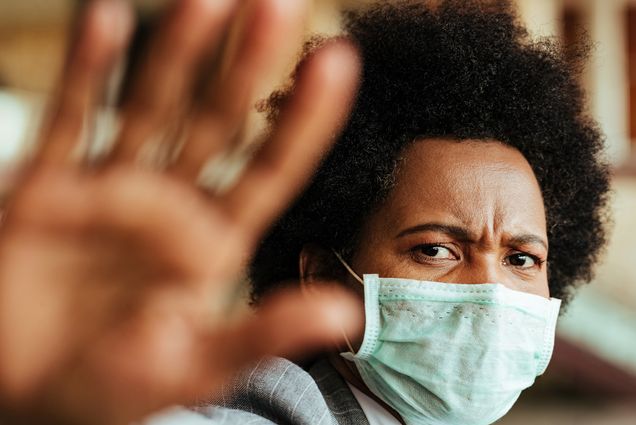 A photo of a woman wearing a mask putting her hand up to prevent someone from coming too close