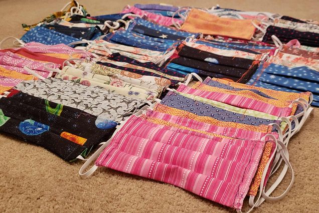 Photo of a pile of multi-colored, hand-sewn masks on a carpet floor.