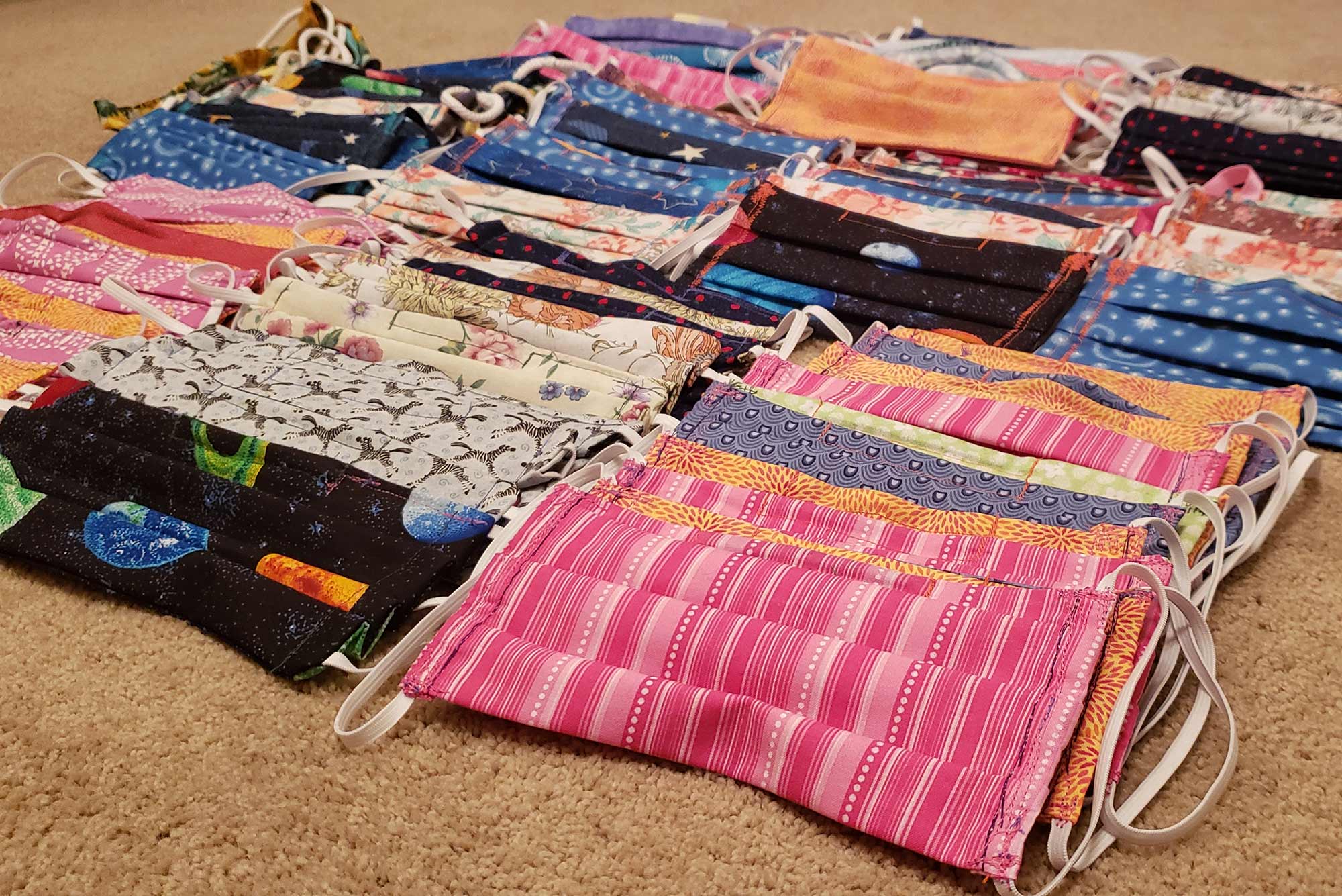 Photo of a pile of multi-colored, hand-sewn masks on a carpet floor.