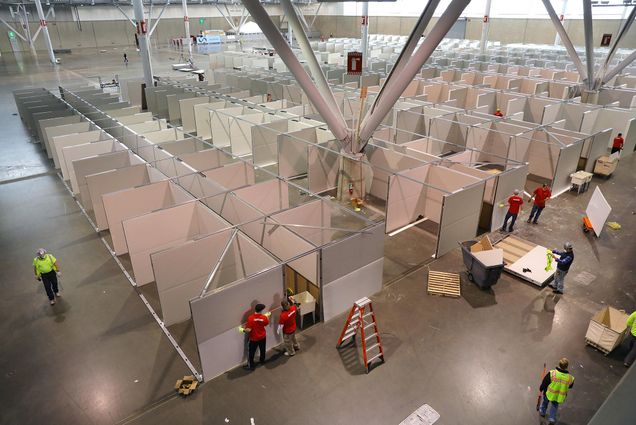 Image of Trade show installers preparing Hall C East of the Boston Convention and Exhibition Center (BCEC) to accommodate 500 beds during the coronavirus pandemic on Apr. 5, 2020. Workers with red shirts set up dividers.