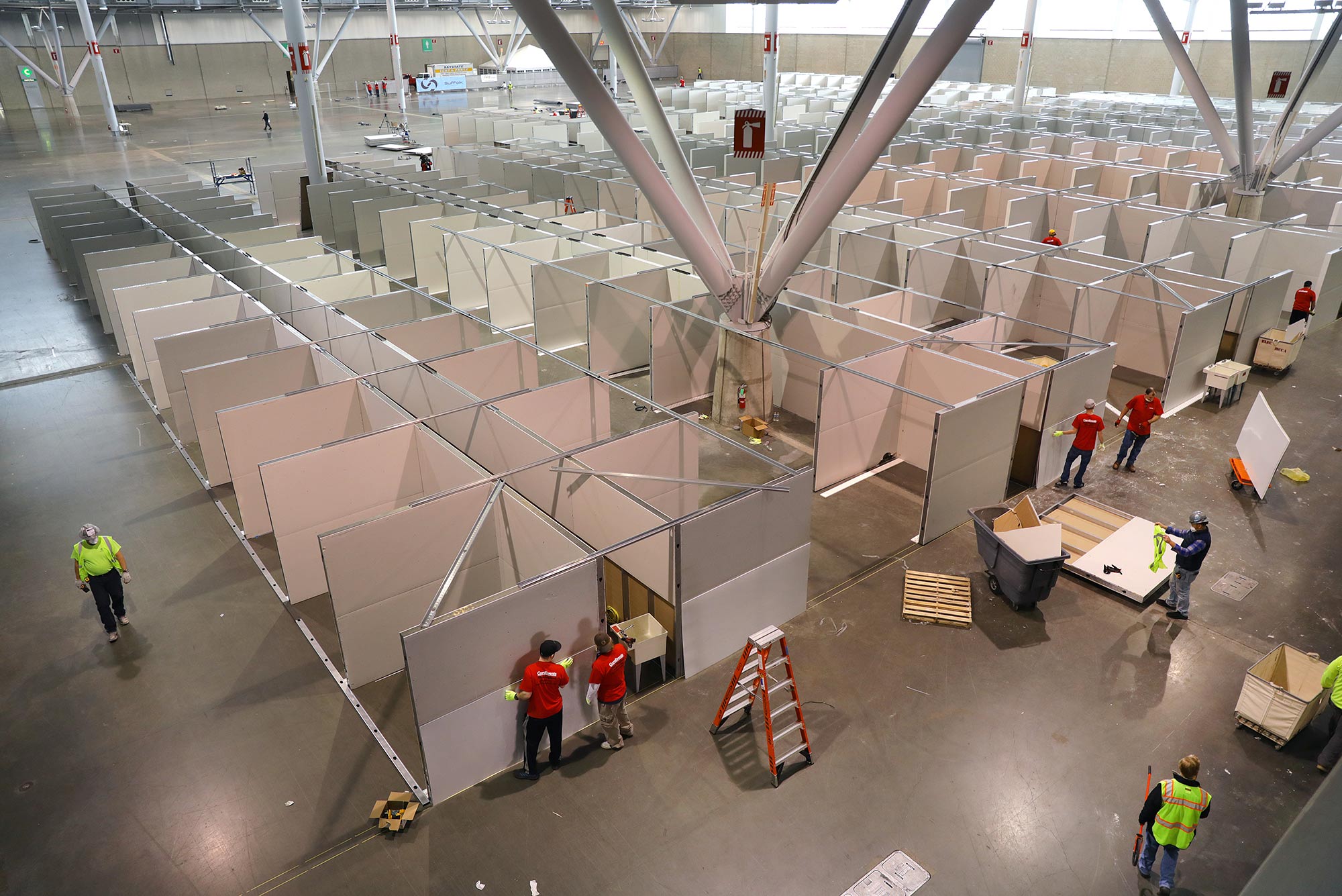 Image of Trade show installers preparing Hall C East of the Boston Convention and Exhibition Center (BCEC) to accommodate 500 beds during the coronavirus pandemic on Apr. 5, 2020. Workers with red shirts set up dividers.