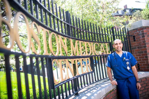 A photo of Massachusetts State Representative Jon Santiago posing in front of a gate that reads "Boston Medical Center"