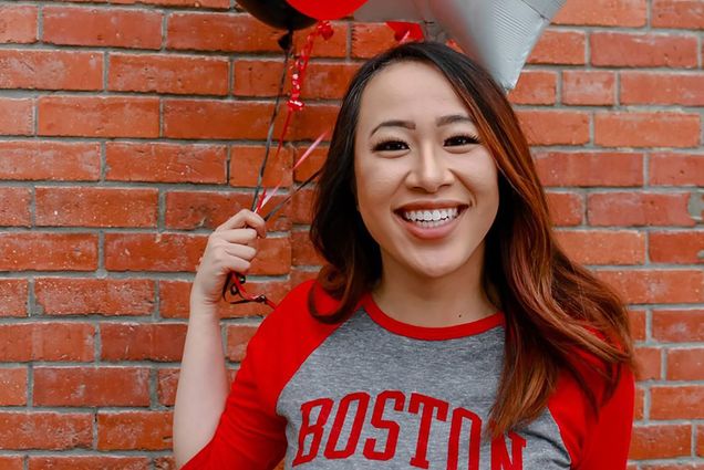 A photo of Geneve Lau holding scarlet and white balloons and wearing a Boston University shirt