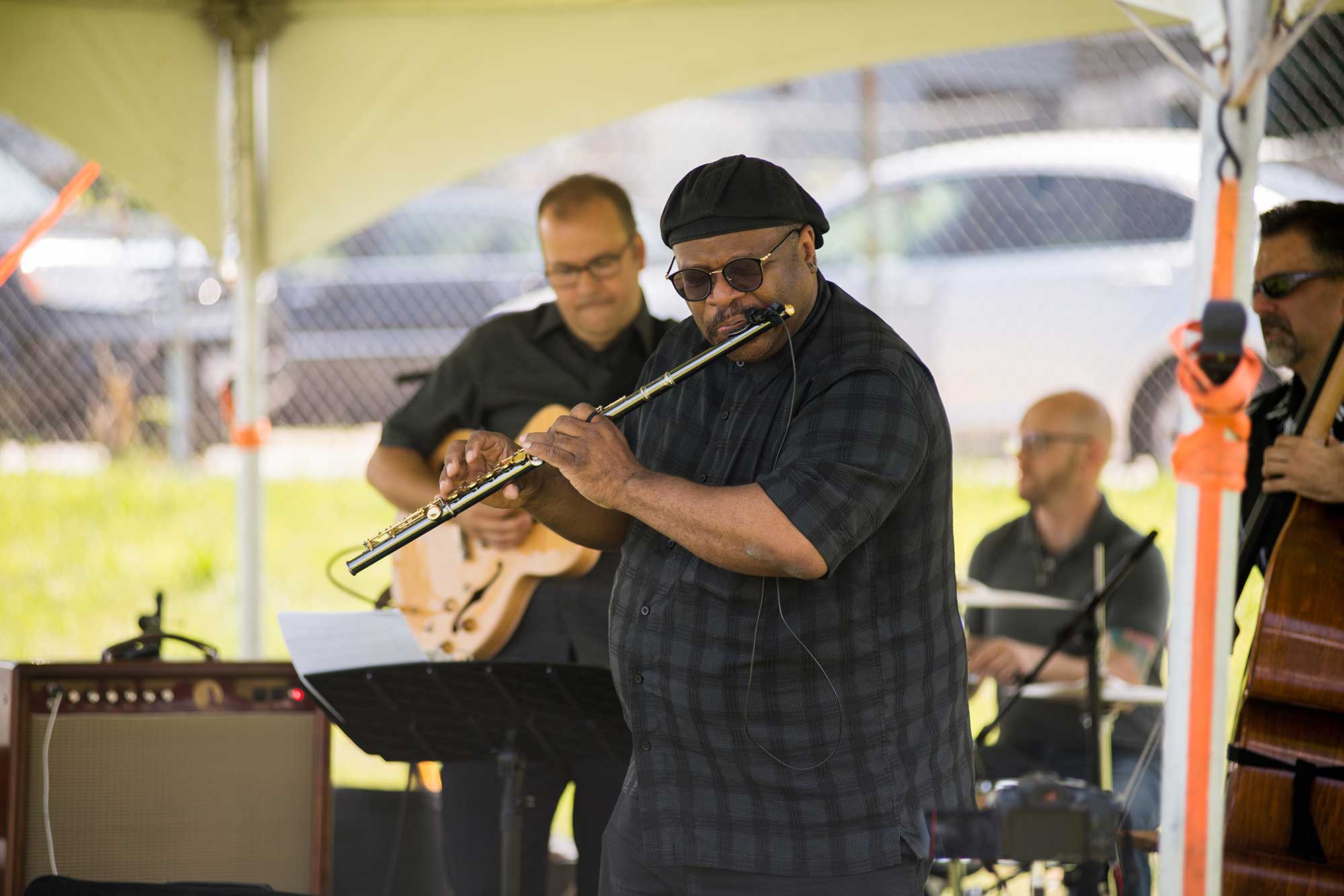 Photo of Lance Martin and The Lance Martin Trio perform during JazzFest in West Roxbury last year. Martin plays a flute, a bassist and drummer are seen in the background at an outdoor venue.