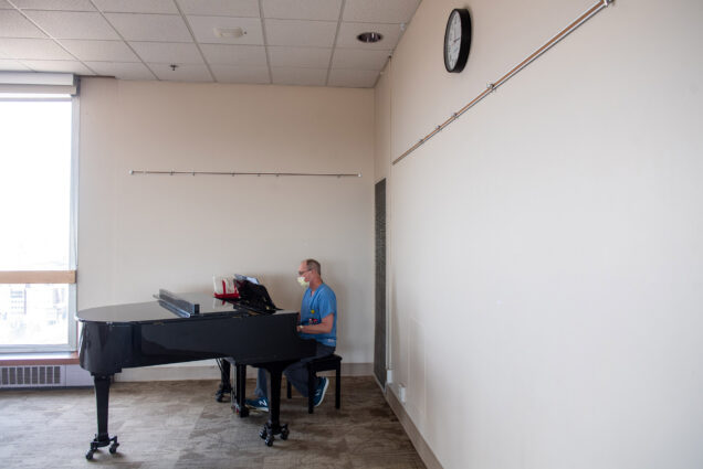 Image of Paul O’Connell, a physician’s assistant at BMC spends his lunch break playing the piano in the Hiebert Lounge at MED on April 29, 2020.