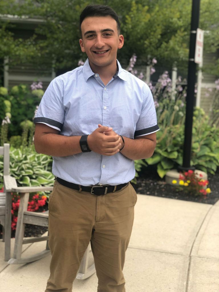 Photo of Greg Levinsky (COM’20) with his hands clasped in front of a garden.