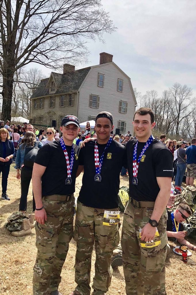 Photo of Ian Saheed (CGS’18, Pardee’20) with two friends; all three wear camouflage pants and running bibs with numbers.