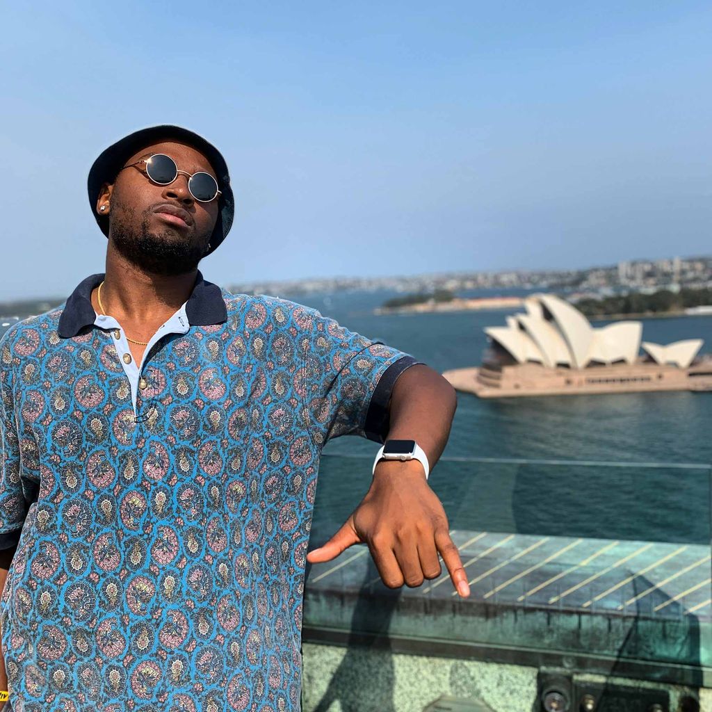 Portrait of Emmanuel Reid (CGS’18, COM’20) in a hat and sunglasses with the Sydney Opera House in the background.