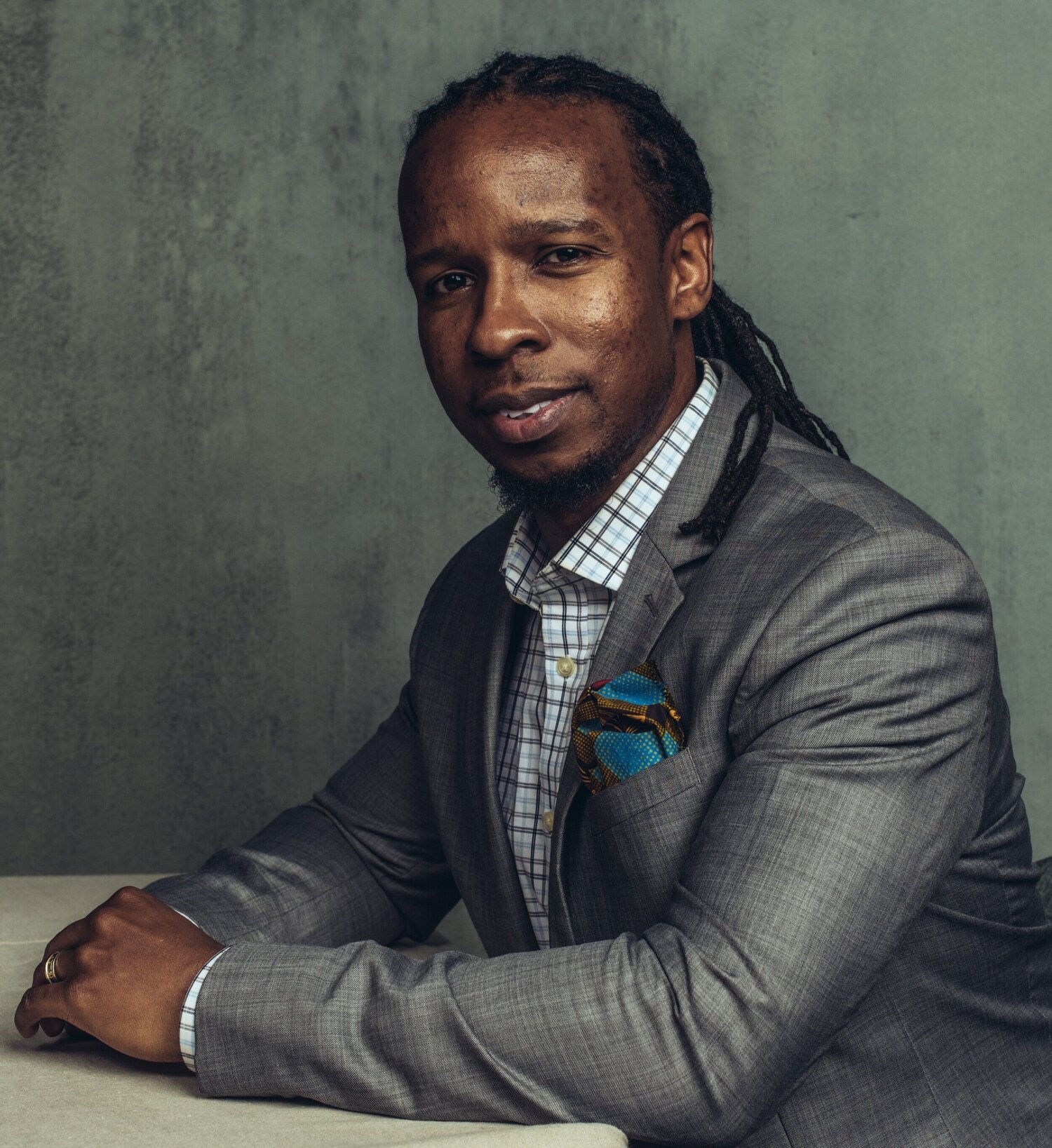 Portait of Ibram X. Kendi in a gray suit with his hands on a desk in front of him. Kendi is a leading historian and author of the bestselling 'How to be an Antiracist.'