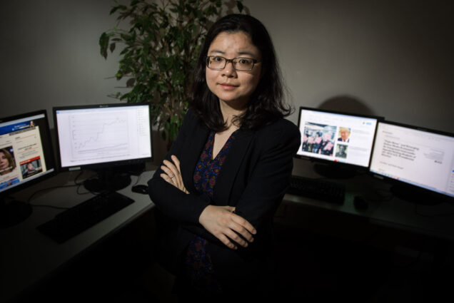 A photo of Lei Guo with her arms crossed in front of a bank of computer monitors