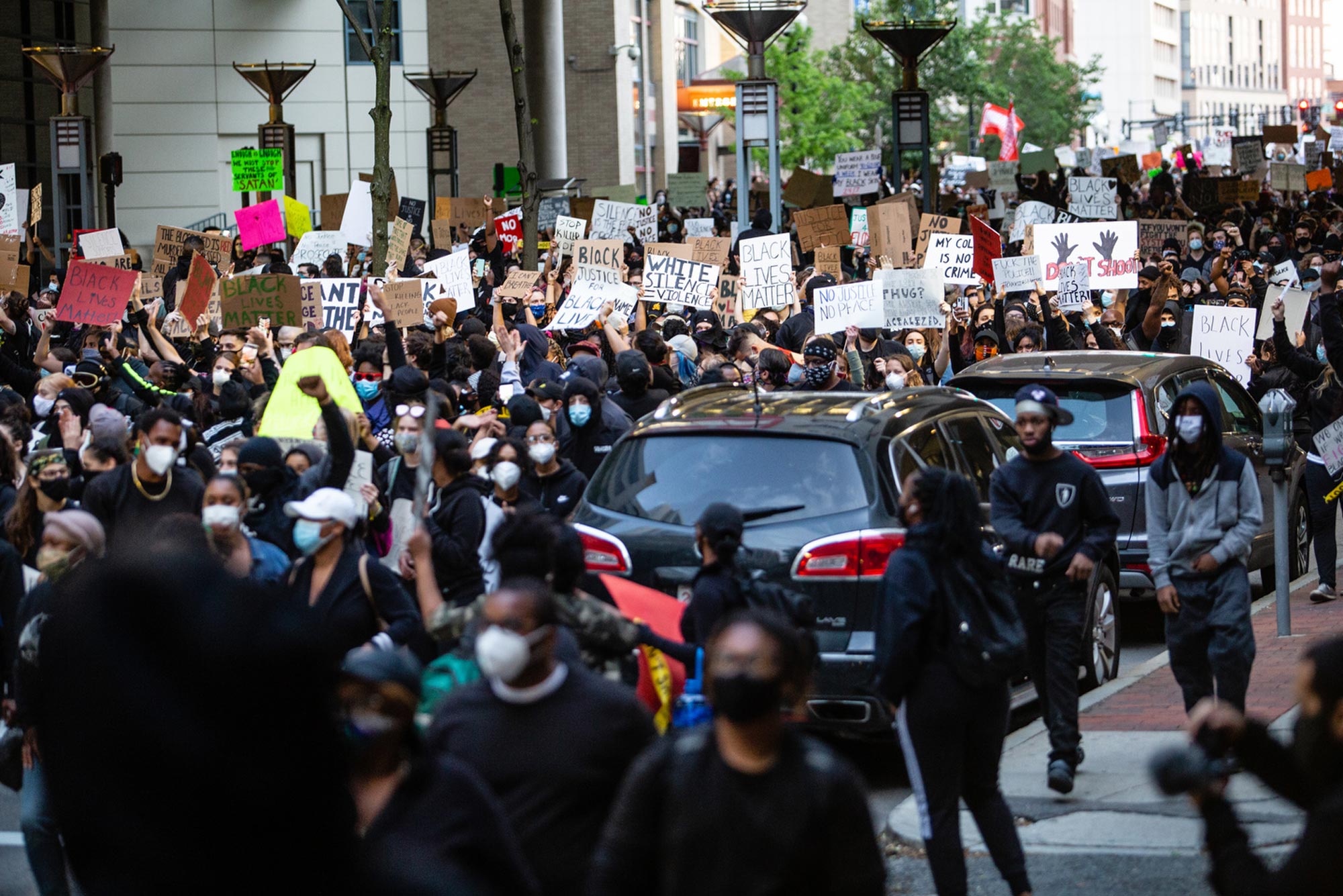 Photo of people took to the streets of Boston on May 31, 2020, protesting the murder of George Floyd. Protesters marched through Tufts Medical Center. Some are seen on sidewalks, a line of parked cars is seen, with most protestors in the streets holding signs.