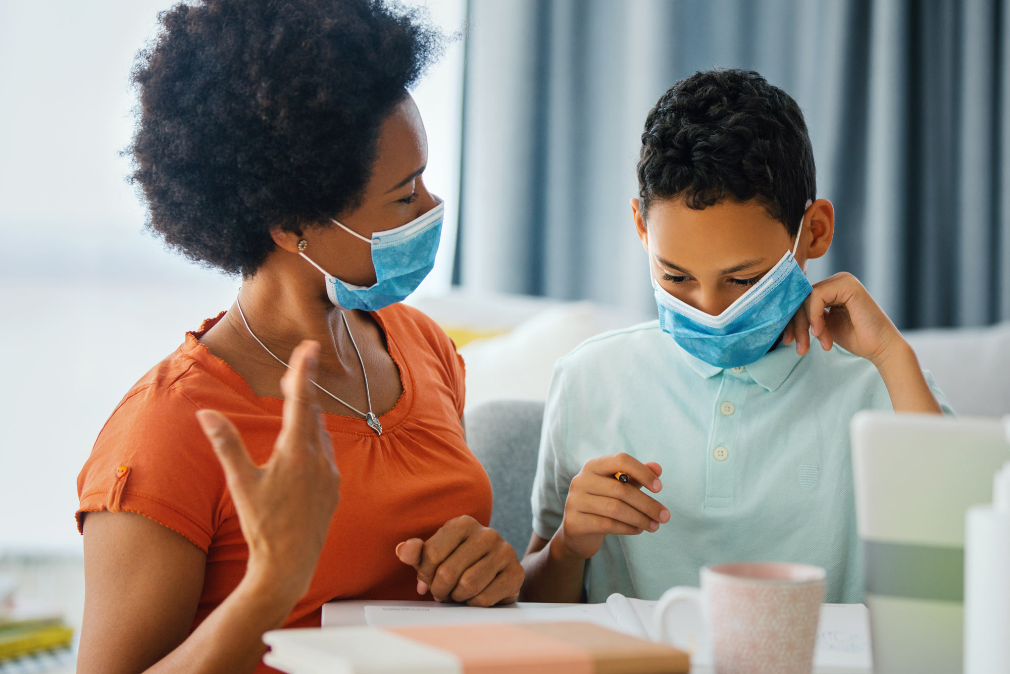 A photo of a woman and child working on schoolwork together at home while wearing masks