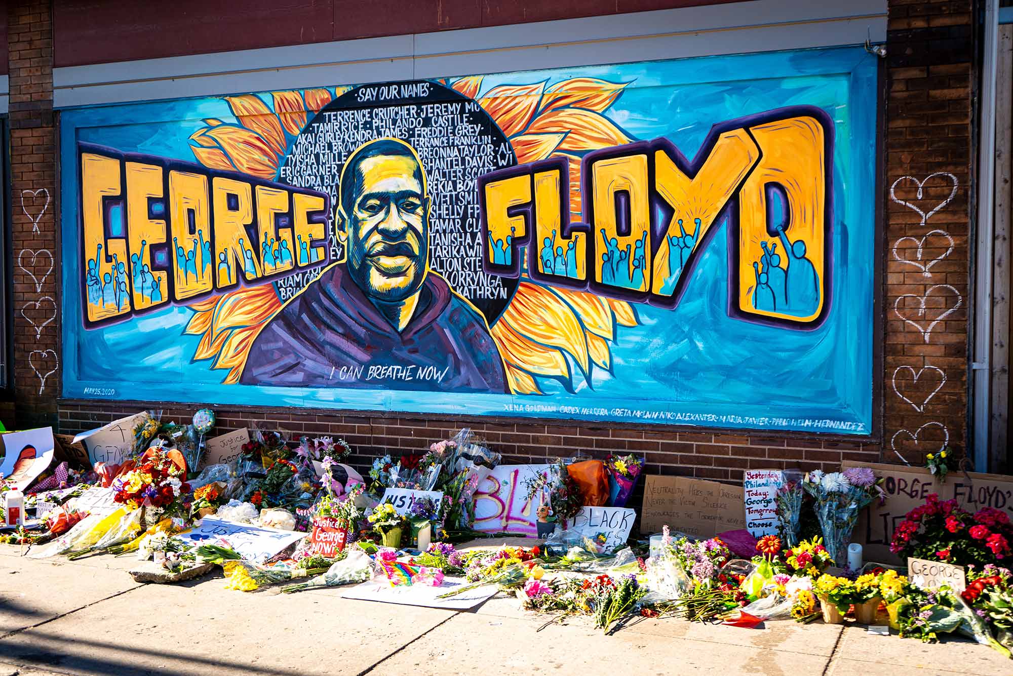 Brightly colored mural honoring George Floyd created during the Black Lives Matter protest in Minneapolis, Minnesota. The mural is a painting of Floyd with a sunflower behind him like a halo. "George Floyd" painted on either side of his portrait.