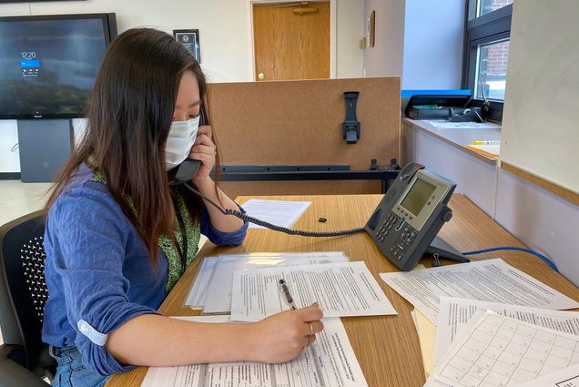 Image of Rinka Murakami (SAR'20, MPH'21) volunteering as a contact tracer for the city of Boston. Murakami wears a mask, writes on some forms, while talking on the phone.