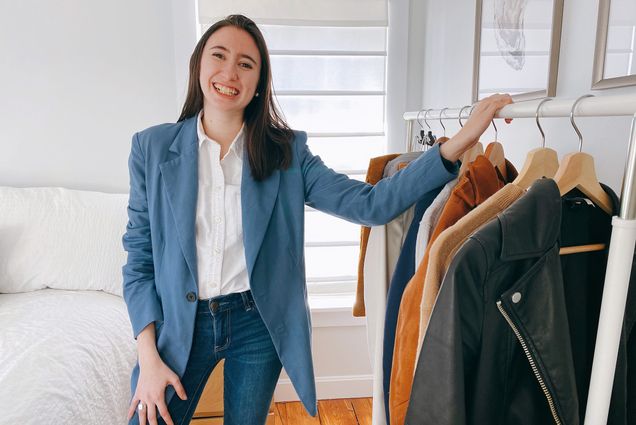 Photo of Sarah Greisdorf, showing off Holdette’s blue blazer, which has six pockets: two on the outside, and four on the inside. Gresidorf rests her hand on a clothes rack to her left.