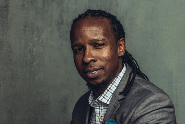 Portait of Ibram X. Kendi in a gray suit with his hands on a desk in front of him. Kendi is a leading historian and author of the bestselling 'How to be an Antiracist.'