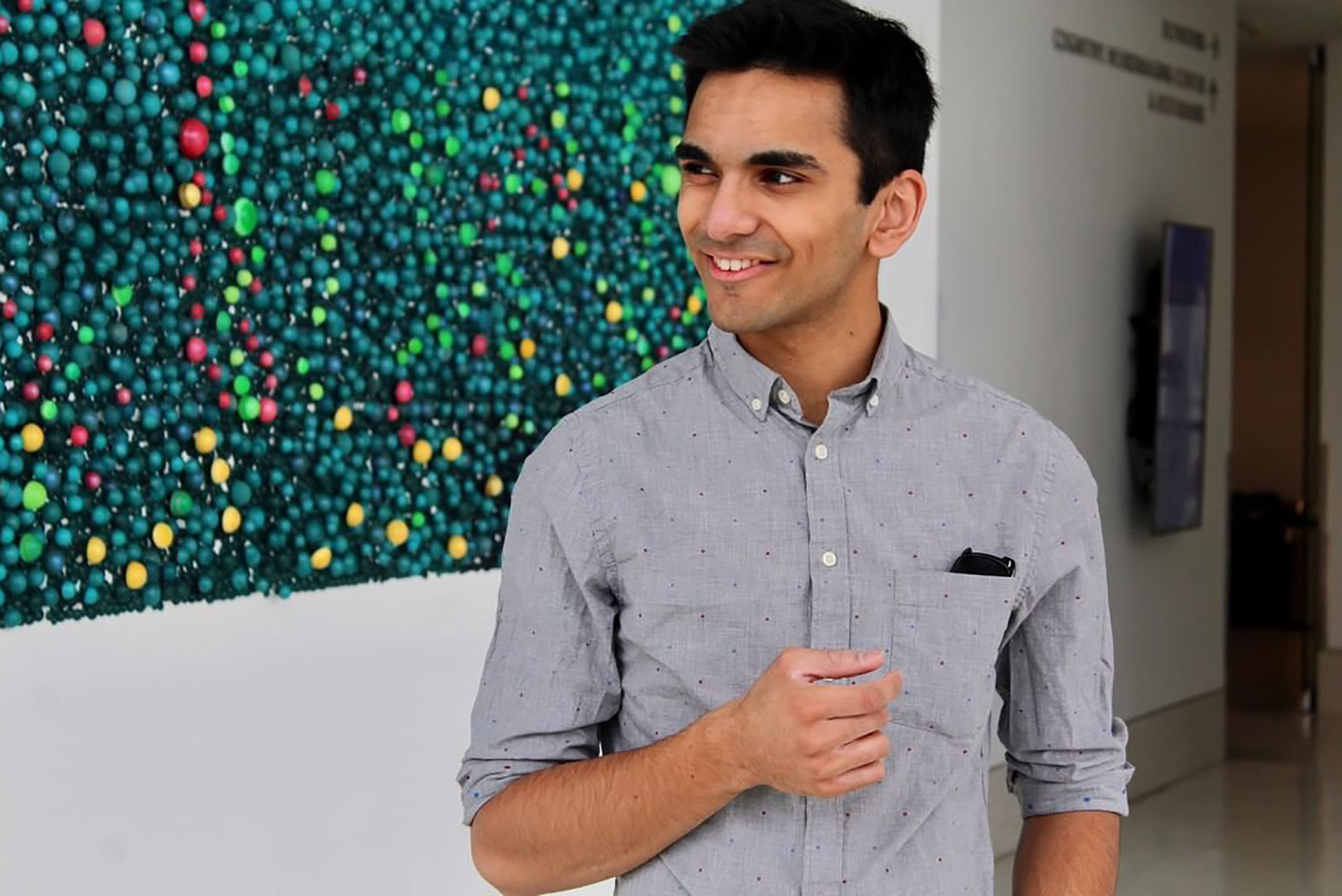 Photo of Hessann Farooqi (CAS’22) smiling in front of a green backdrop with green, red and yellow spots.