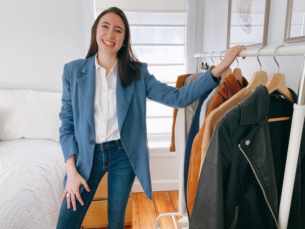 Photo of Sarah Greisdorf, showing off Holdette’s blue blazer, which has six pockets: two on the outside, and four on the inside. Gresidorf rests her hand on a clothes rack to her left.
