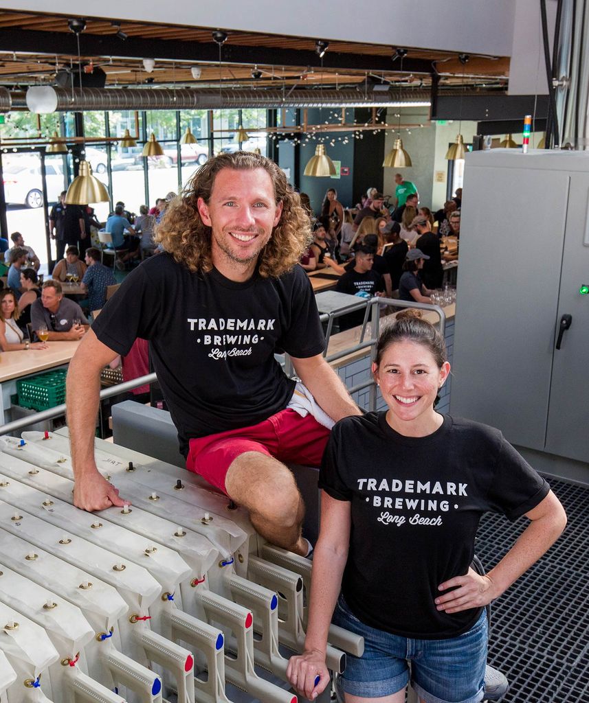 Photo of Ilana Steffen (CGS’06, SHA’08) and her husband, Sterling, opened their Long Beach, Calif., brewery, Trademark Brewing, in June 2019. They quickly turned to producing hand sanitizer during the pandemic. In the photo, they both wear black shirts and a crowd of brewery-goers is seen in the background.