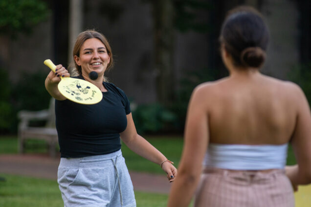 Photo of Veronica Fadel (CAS’20), facing, and Mia Touma (CAS’21) playing paddleballon the BU beach. Fadel smiles and hits a small black ball back to Touma.