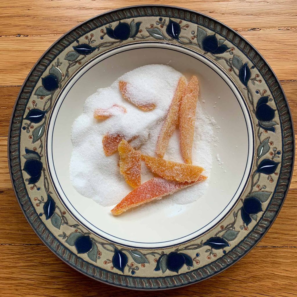 Orange peels tossed in sugar in a bowl with a blue and green floral border on wood.