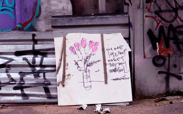 Photo of a hand drawn image of a vase with pink flowers against the backdrop of a graffiti covered wall. "You are all that makes the day beautiful" is written to the right of the drawing.