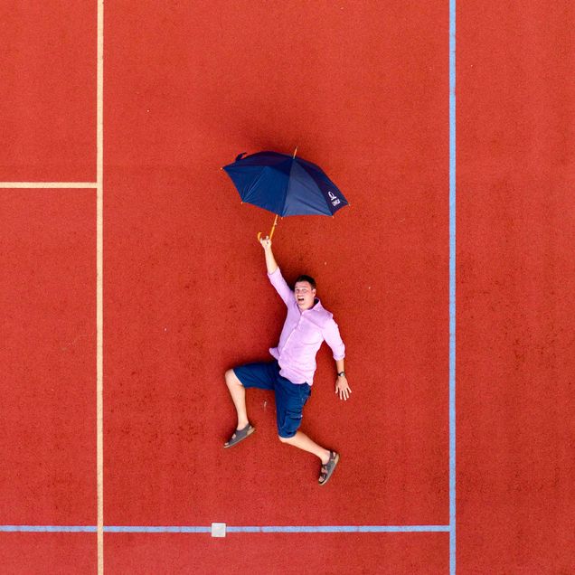 Photo of a man in a pink shirt and blue shirt laying on the ground with an umbrella in his hands. His body is framed by white lines on the ground.