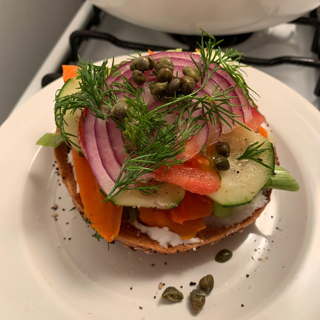 A bagel with vegan cream cheese and homemade carrot “lox" on a white plate.