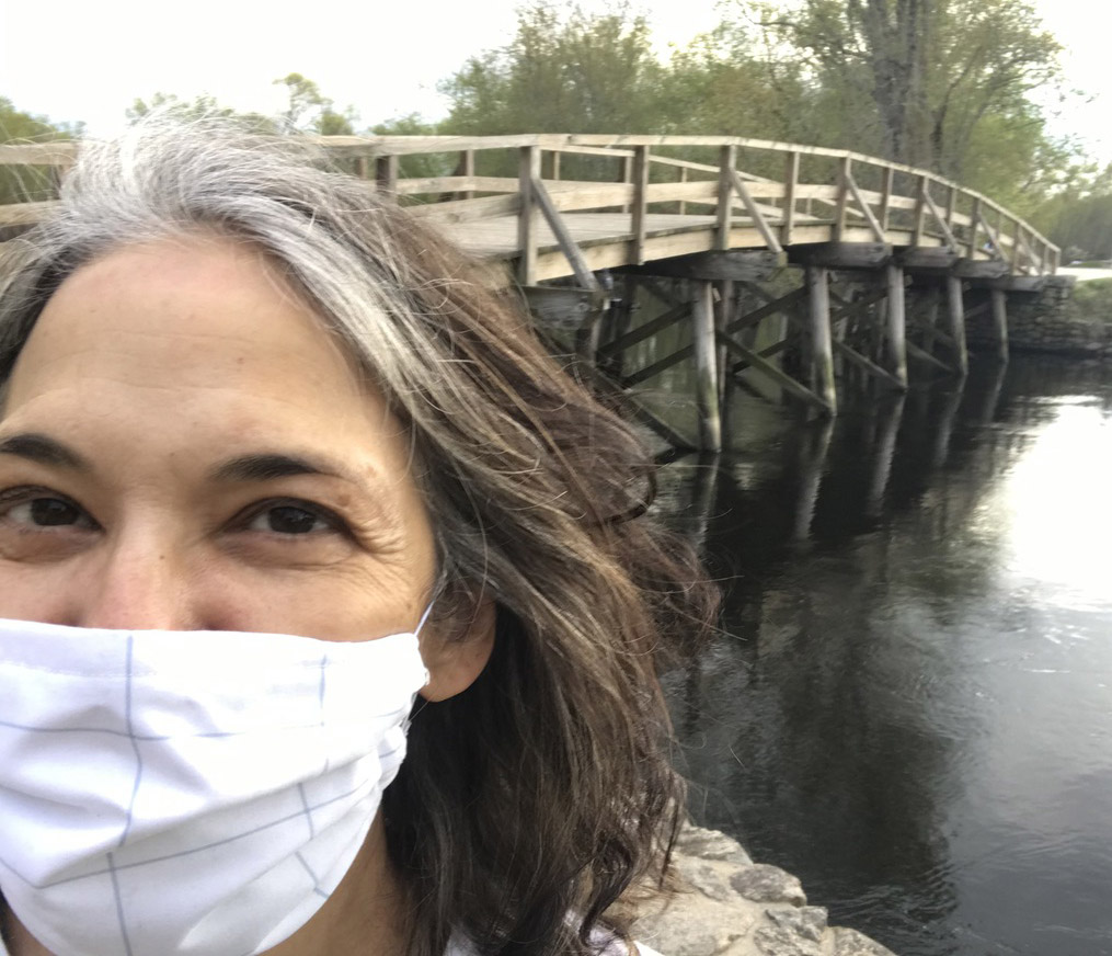 Melinda Lopez wearing a PPE mask standing in front of a bridge