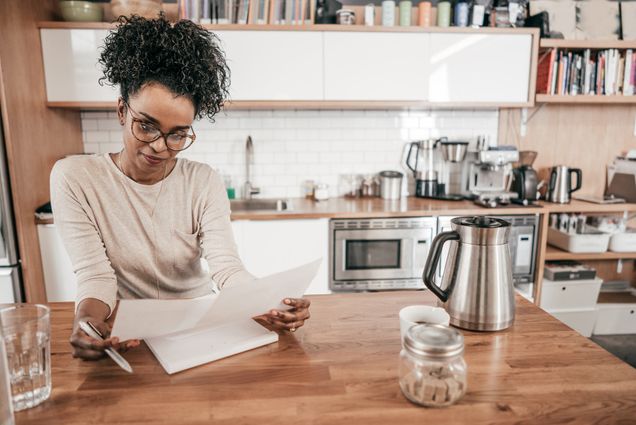 A woman sitting at a kitchen counter looking at a piece of paper