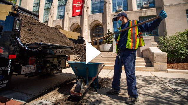 A BU employee shovels mulch from the back of a truck into a wheelbarrow in front of the Tsai Performance Center. A white video play button is over the image.